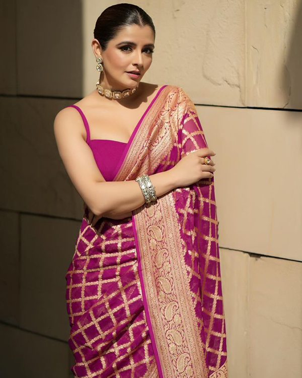 Natasha Luthra poses in a magenta saree with gold patterns, wearing a statement choker necklace, matching earrings, and silver bangles.