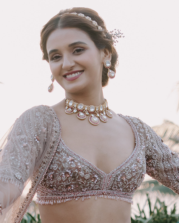 Shakti Mohan smiles wearing a gold choker, matching earrings, and a headpiece, with an intricately embroidered blouse.