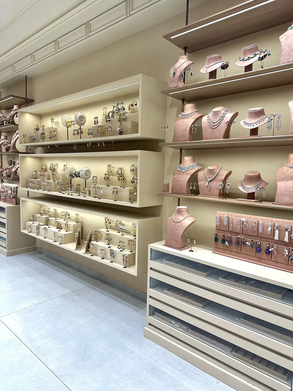 A well-lit jewelry store interior displays a wide array of earrings and necklaces on illuminated wall shelves and display cases, featuring a soft, neutral color scheme.