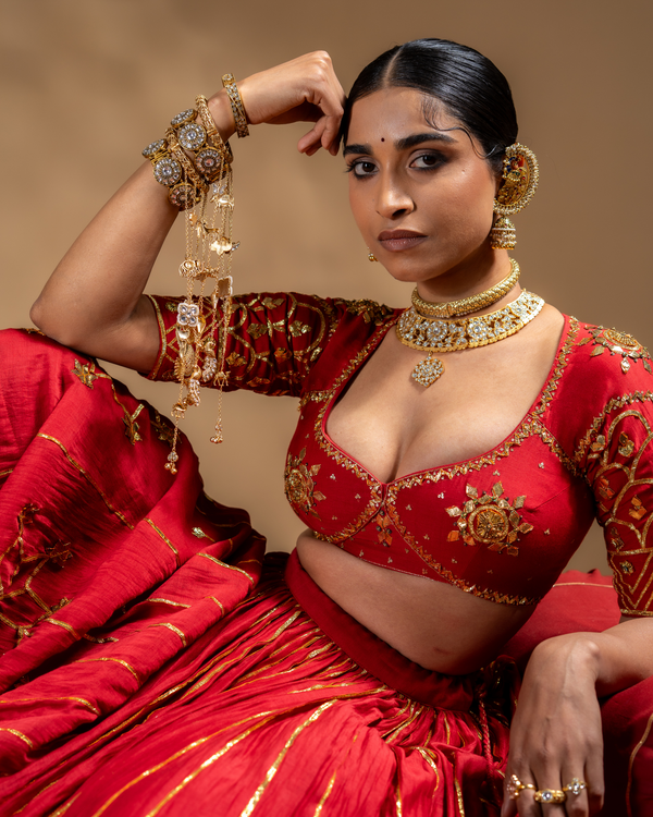 Woman in traditional red and gold outfit with jewelry against a brown background