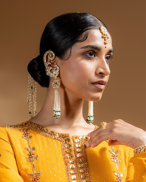 Woman wearing traditional jewelry with a yellow outfit against a brown background