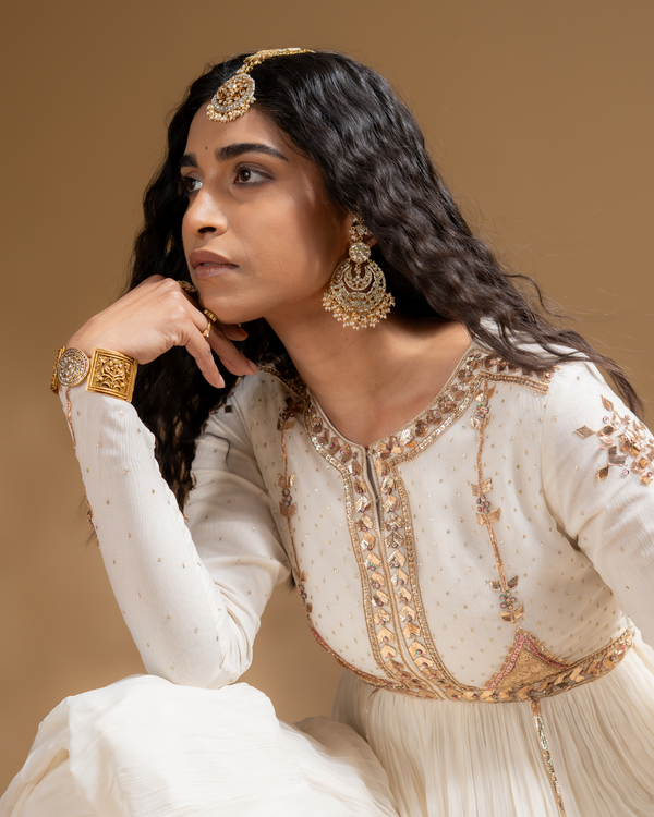 Woman in traditional outfit with gold embroidery and jewelry against a brown background
