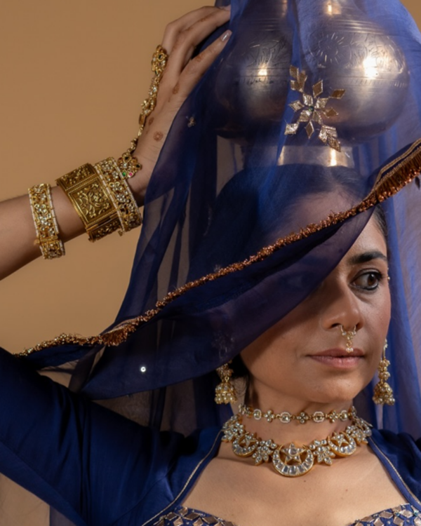 Woman wearing a blue saree with gold jewelry against a beige background