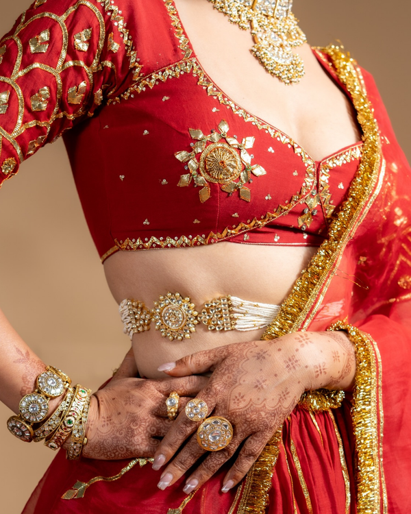 Red saree with gold embroidery and jewelry on a beige background