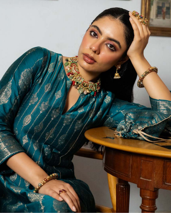 Woman in a blue saree with gold patterns sitting at a wooden table.