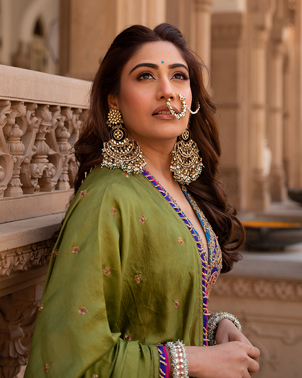 Surbhi Chandna poses in traditional attire, adorned with large ornate jhumka earrings and a kundan nose ring, looking upwards.